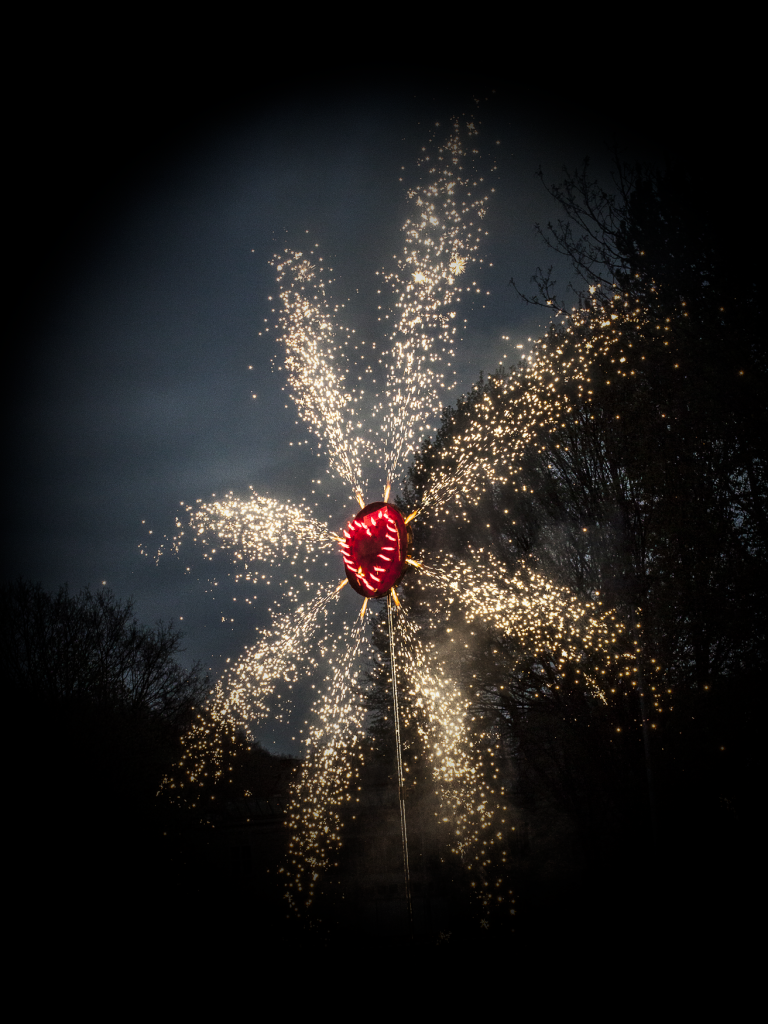 Leuchtende Feuerwerksblüte mit einem roten Herz in der Mitte auf dunklem Hintergrund.