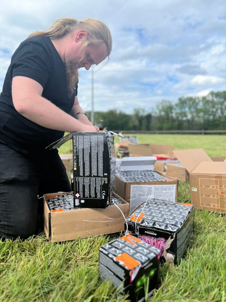 Person mit langen Haaren arbeitet auf einer Wiese und sortiert elektronische Geräte.